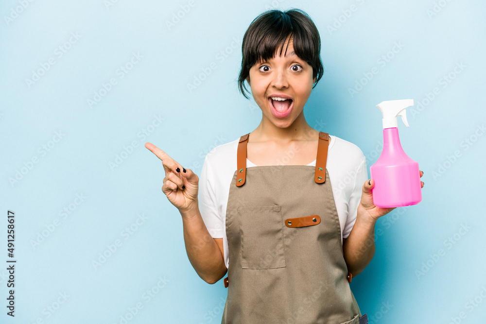 Young hispanic gardener woman holding a hand sprayer isolated on blue background pointing to the side Young hispanic gardener woman holding a hand sprayer isolated on blue background pointing to the side