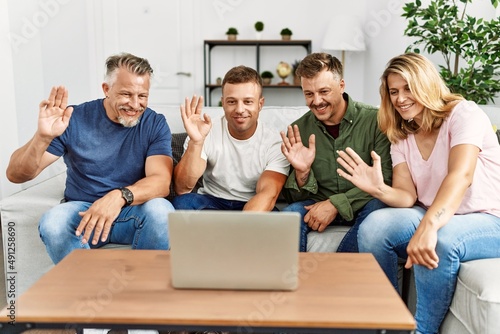 Group of middle age friends having video call using laptop sitting on the sofa at home.