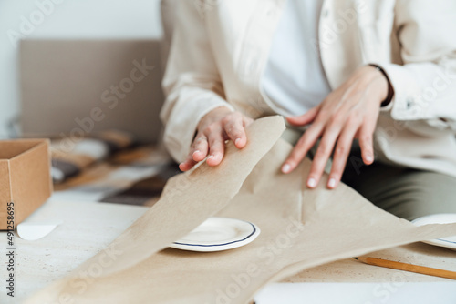 Craftswoman packing ceramic plate in wrapping paper for shipping