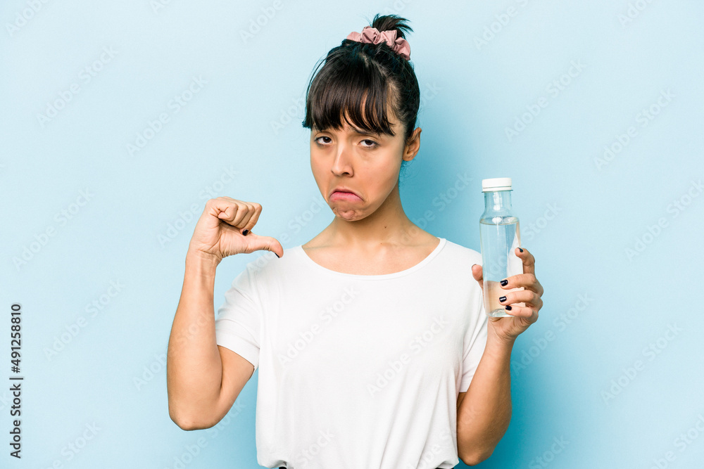 Young hispanic woman holding a bottle of water isolated on blue background feels proud and self confident, example to follow. Young hispanic woman holding a bottle of water isolated on blue background feels proud and self confident, example to follow.