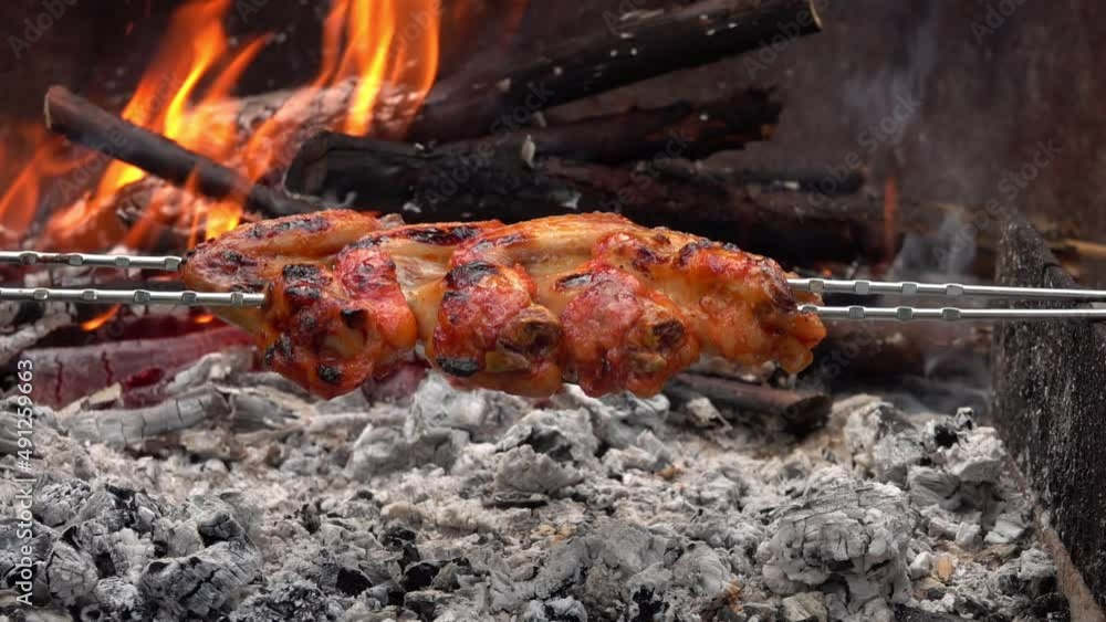 Mouth-watering spicy chicken wings on the skewers are frying above the open fire Mouth-watering spicy chicken wings on the skewers are frying above the open fire