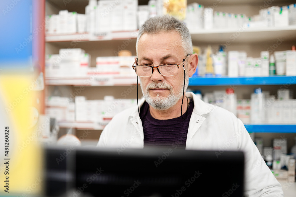Pharmacist wearing eyeglasses using computer in pharmacy Pharmacist wearing eyeglasses using computer in pharmacy