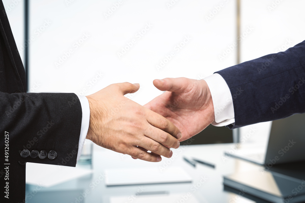 Two businessmen shake hands in sunny modern office, partnership concept, close up