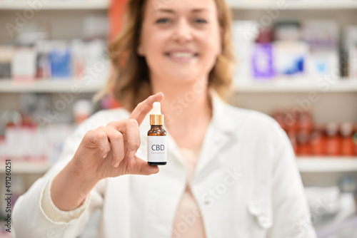 Smiling pharmacist holding bottle of cannabis oil at pharmacy store photo