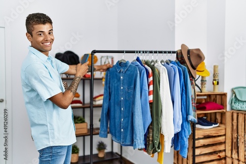 Young hispanic man shopping taking pictures to clothes at retail shop