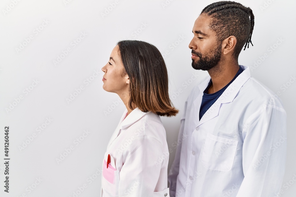 Young hispanic doctors standing over white background looking to side, relax profile pose with natural face and confident smile. Young hispanic doctors standing over white background looking to side, relax profile pose with natural face and confident smile.