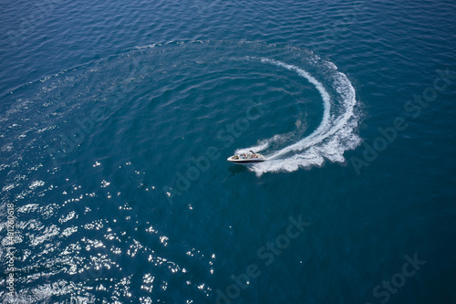 One boat on blue water drone view. Modern boat in a circular motion making a trail on the water. Top view. Boat in turn fast moving aerial view.