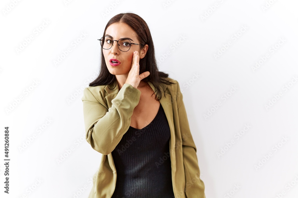 Young brunette woman standing over isolated background hand on mouth telling secret rumor, whispering malicious talk conversation Young brunette woman standing over isolated background hand on mouth telling secret rumor, whispering malicious talk conversation