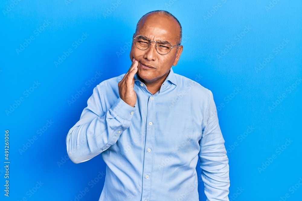 Middle age latin man wearing casual clothes and glasses touching mouth with hand with painful expression because of toothache or dental illness on teeth. dentist Middle age latin man wearing casual clothes and glasses touching mouth with hand with painful expression because of toothache or dental illness on teeth. dentist