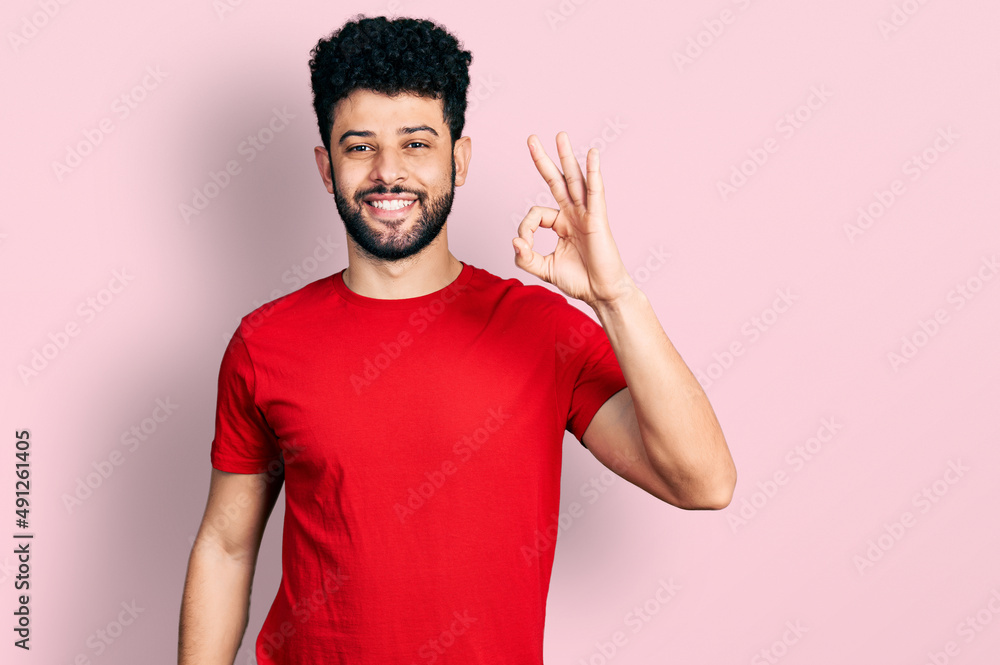 Young arab man with beard wearing casual red t shirt smiling positive doing ok sign with hand and fingers. successful expression. Young arab man with beard wearing casual red t shirt smiling positive doing ok sign with hand and fingers. successful expression.