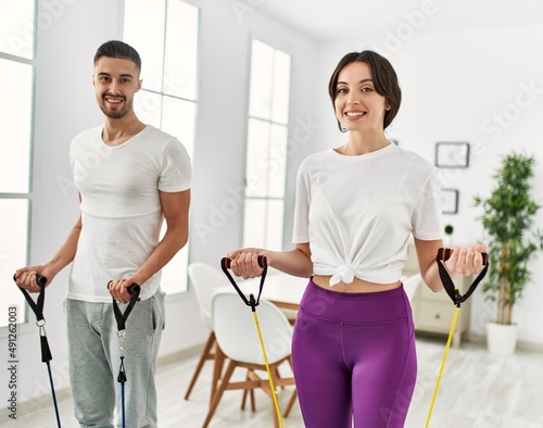 Young hispanic couple doing strong exercise using elastic band at home