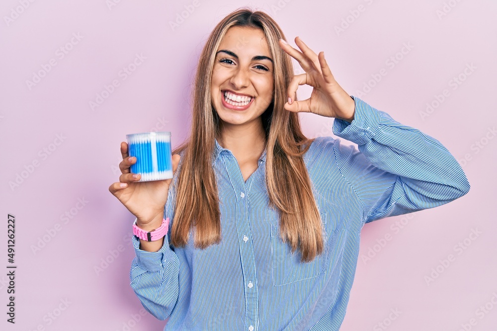 Beautiful hispanic woman holding earwax cotton removers doing ok sign with fingers, smiling friendly gesturing excellent symbol Beautiful hispanic woman holding earwax cotton removers doing ok sign with fingers, smiling friendly gesturing excellent symbol