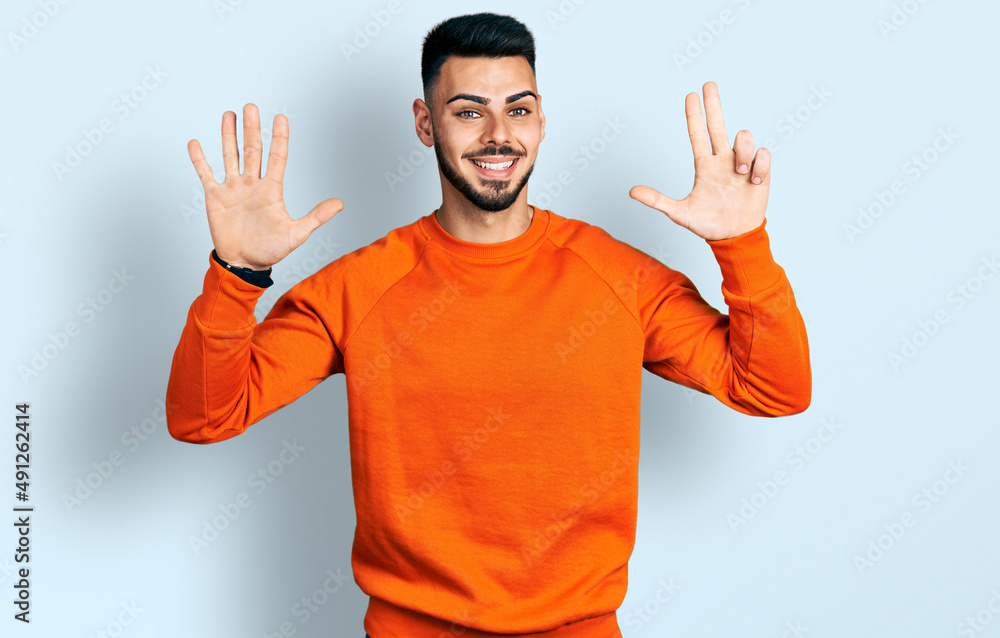 Fototapeta premium Young hispanic man with beard wearing casual orange sweater showing and pointing up with fingers number eight while smiling confident and happy.