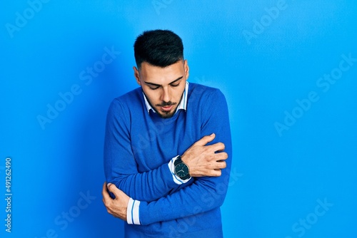 Young hispanic man with beard wearing casual blue sweater shaking and freezing for winter cold with sad and shock expression on face