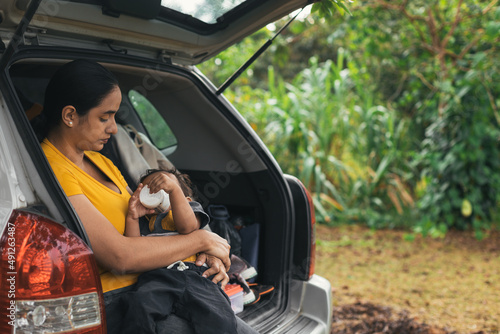 mom giving her baby a bottle in the back of the vehicle, mom and her son in a natural environment © Dionisio