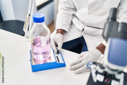 Young african american man wearing scientist uniform weighing test tube at laboratory