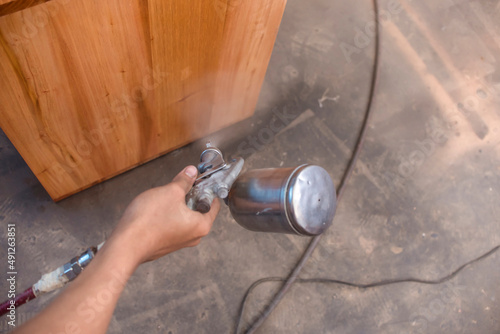 Canvas Print A handyman sprays lacquer wood finish on a shelf or cabinet