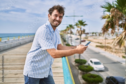 Young hispanic man smiling happy using smartphone at the promenade.
