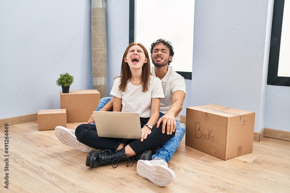 Young couple using laptop at new home angry and mad screaming frustrated and furious, shouting with anger. rage and aggressive concept. Young couple using laptop at new home angry and mad screaming frustrated and furious, shouting with anger. rage and aggressive concept.