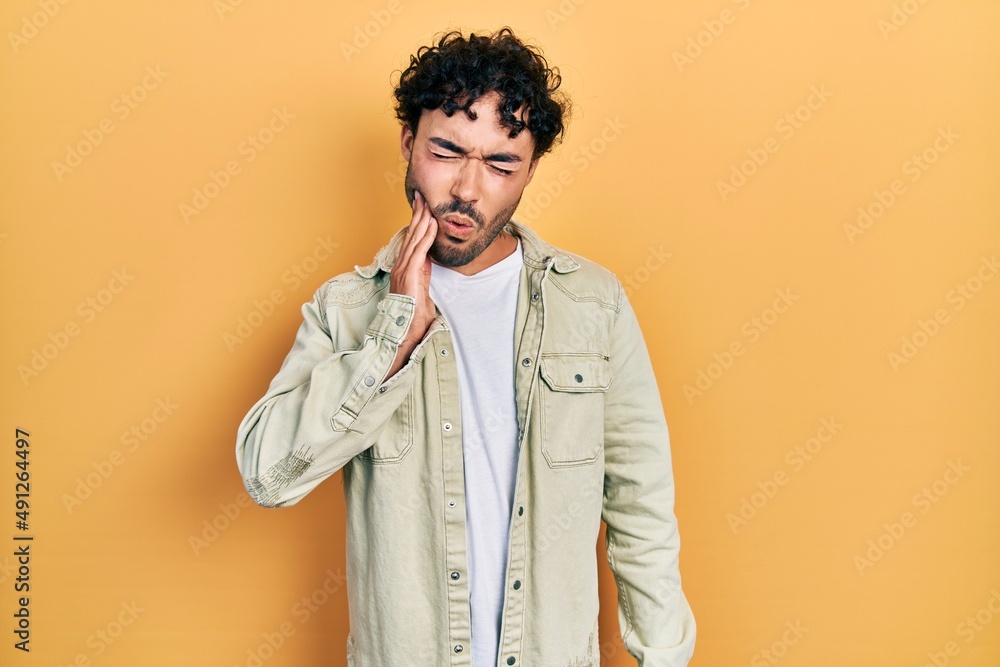 Young hispanic man wearing casual clothes touching mouth with hand with painful expression because of toothache or dental illness on teeth. dentist Young hispanic man wearing casual clothes touching mouth with hand with painful expression because of toothache or dental illness on teeth. dentist