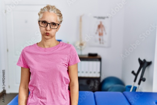 Middle age blonde woman at pain recovery clinic puffing cheeks with funny face. mouth inflated with air  crazy expression.