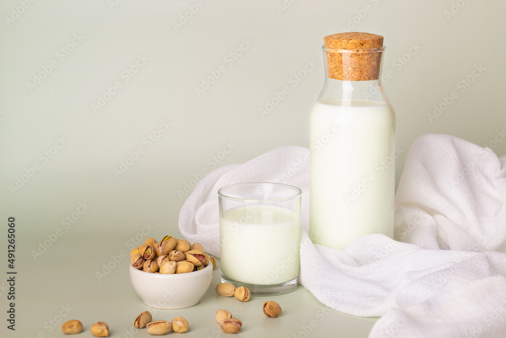 Fresh pistachio milk in a glass bottle and cup, set against a neutral backdrop with scattered pistachios.