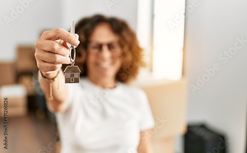 Middle age hispanic woman smiling happy holding key of house at new home