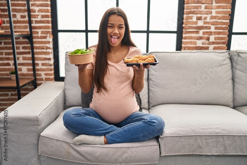 Foto Young pregnant woman craving for food at home sticking tongue out happy with funny expression