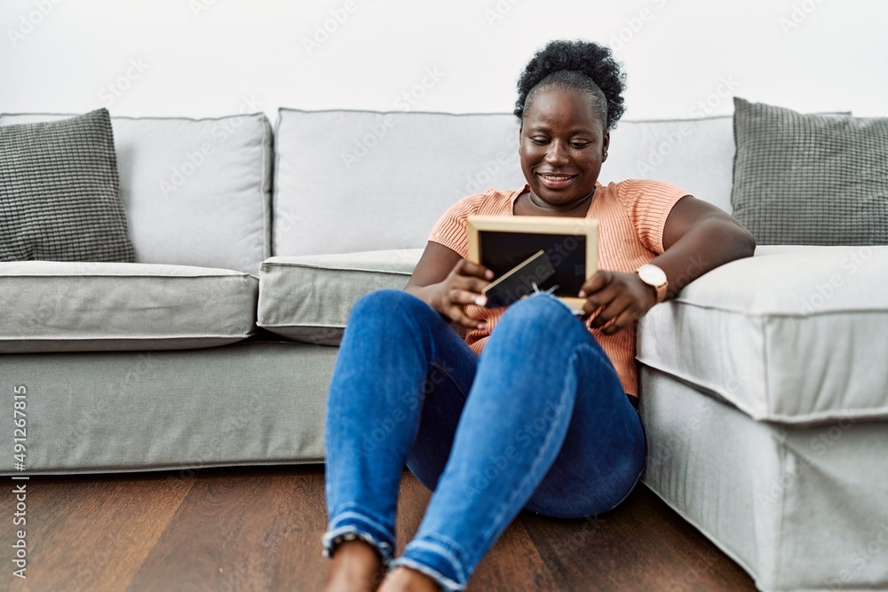 Young african american woman looking photo sitting on the floor at home Young african american woman looking photo sitting on the floor at home