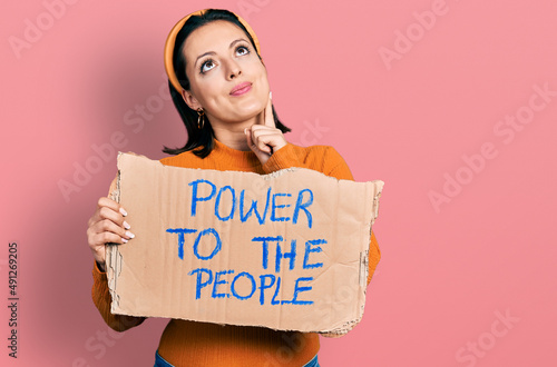 Young hispanic girl holding power to the people banner serious face thinking about question with hand on chin, thoughtful about confusing idea © Krakenimages.com