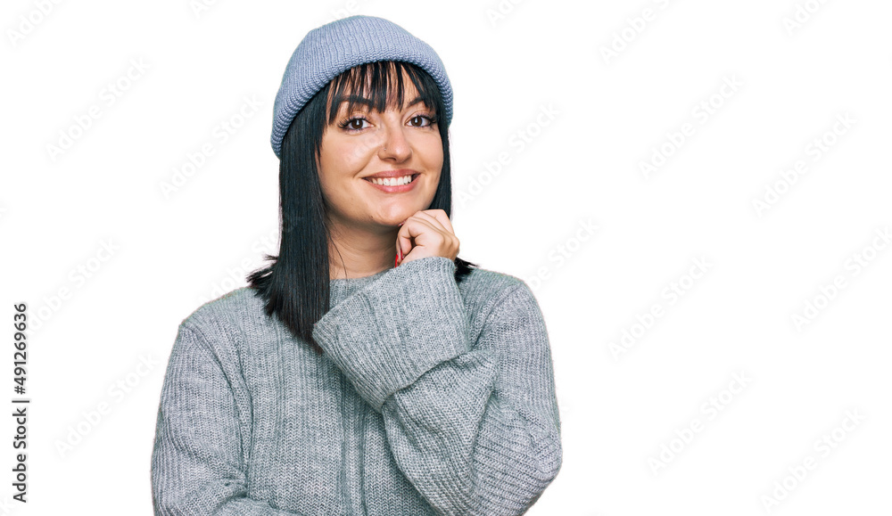 Young hispanic woman wearing cute wool cap looking confident at the camera with smile with crossed arms and hand raised on chin. thinking positive. Young hispanic woman wearing cute wool cap looking confident at the camera with smile with crossed arms and hand raised on chin. thinking positive.