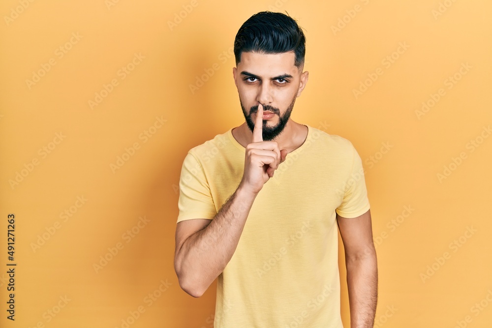 Handsome man with beard wearing casual yellow t shirt asking to be quiet with finger on lips. silence and secret concept. Handsome man with beard wearing casual yellow t shirt asking to be quiet with finger on lips. silence and secret concept.
