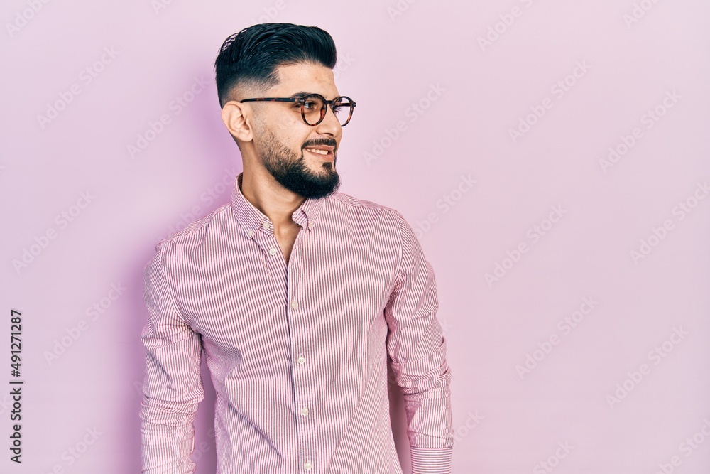 Handsome man with beard wearing casual shirt and glasses looking away to side with smile on face, natural expression. laughing confident. Handsome man with beard wearing casual shirt and glasses looking away to side with smile on face, natural expression. laughing confident.