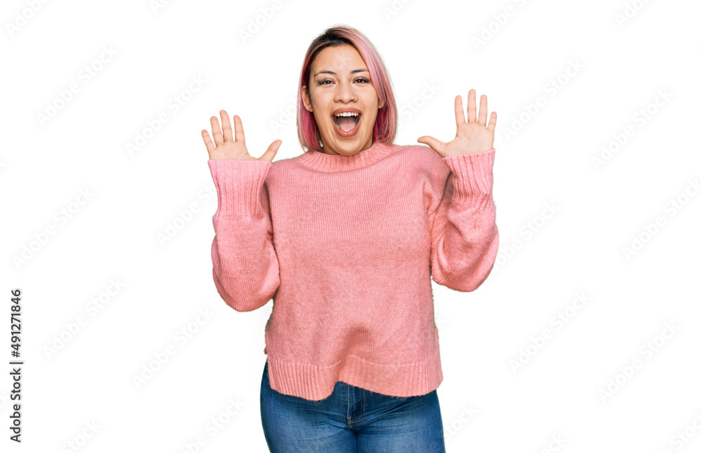 Hispanic woman with pink hair wearing casual winter sweater celebrating crazy and amazed for success with arms raised and open eyes screaming excited. winner concept Hispanic woman with pink hair wearing casual winter sweater celebrating crazy and amazed for success with arms raised and open eyes screaming excited. winner concept