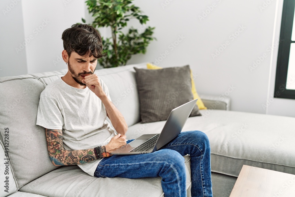 Hispanic man with beard sitting on the sofa feeling unwell and coughing as symptom for cold or bronchitis. health care concept.