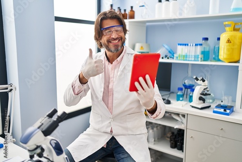 Handsome middle age man working at scientist laboratory doing video call smiling happy and positive  thumb up doing excellent and approval sign