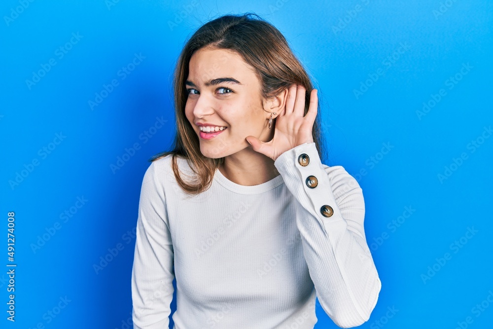 Young caucasian girl wearing casual clothes smiling with hand over ear listening and hearing to rumor or gossip. deafness concept. Young caucasian girl wearing casual clothes smiling with hand over ear listening and hearing to rumor or gossip. deafness concept.