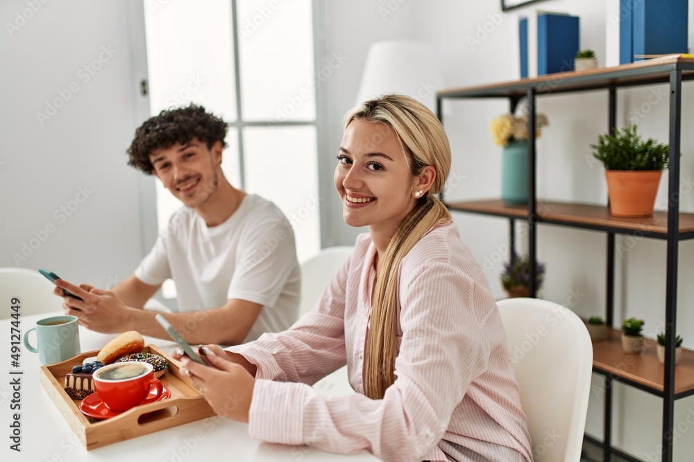 Fototapeta premium Young couple having breakfast using smartphone at home.