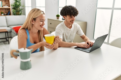 Young couple using laptop and drinking coffee at home.