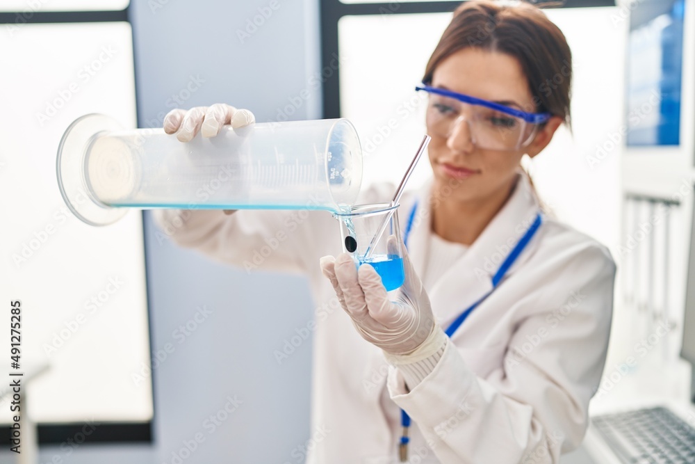 Young hispanic woman wearing scientist uniform measuring liquid at laboratory Young hispanic woman wearing scientist uniform measuring liquid at laboratory