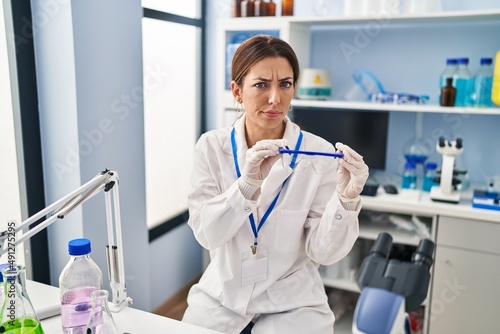 Young brunette woman working at scientist laboratory wearing safety glasses skeptic and nervous, frowning upset because of problem. negative person.