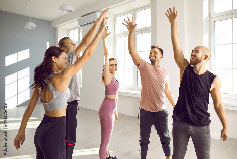 Fototapeta premium Team of cheerful young people motivating each other before an indoor sports workout at the gym. Group of happy, energetic, enthusiastic men and women determined to achieve a common fitness goal