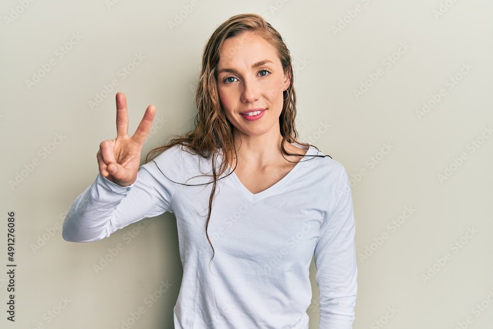 Young blonde woman wearing casual clothes showing and pointing up with fingers number two while smiling confident and happy. Young blonde woman wearing casual clothes showing and pointing up with fingers number two while smiling confident and happy.