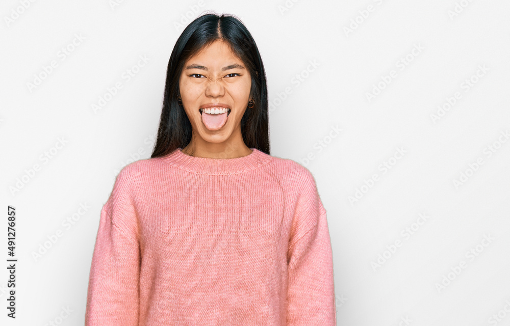 Fototapeta premium Beautiful young asian woman wearing casual winter sweater sticking tongue out happy with funny expression. emotion concept.