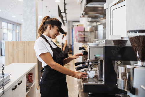 Print op canvas Beautiful and happy young female worker working in a bakery or fast food restaurant and using coffee machine