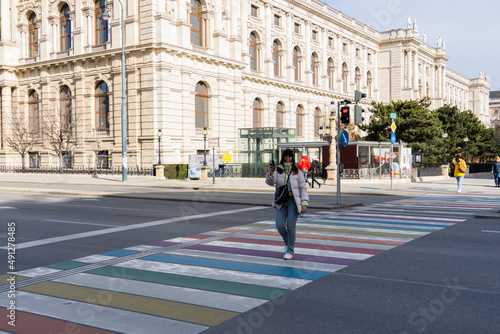 woman with phone crossing rainbow flag zebra crossing in vienna
