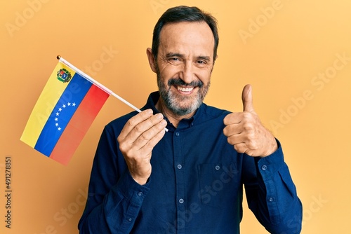 Middle age hispanic man holding venezuelan flag smiling happy and positive, thumb up doing excellent and approval sign photo