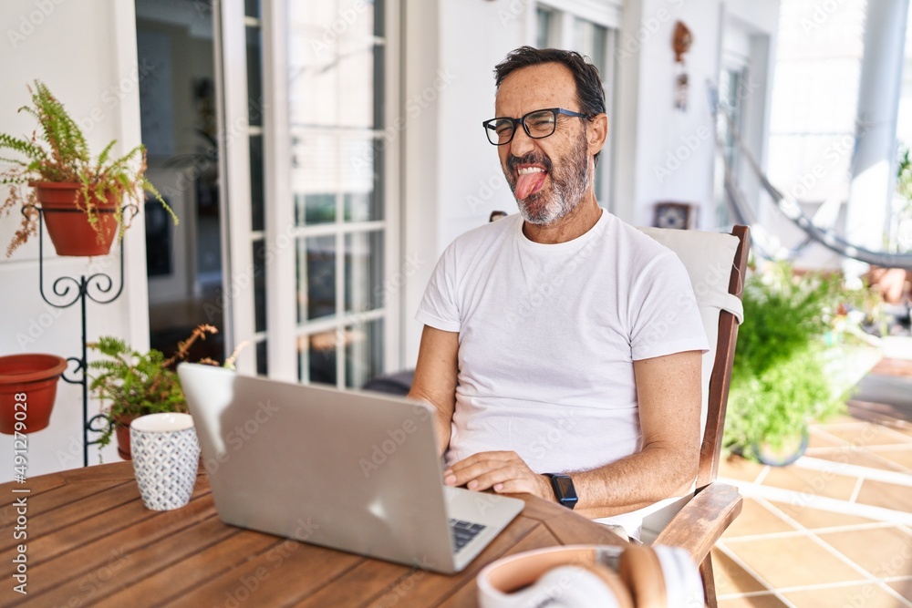 Middle age man using computer laptop at home sticking tongue out happy with funny expression. emotion concept. Middle age man using computer laptop at home sticking tongue out happy with funny expression. emotion concept.