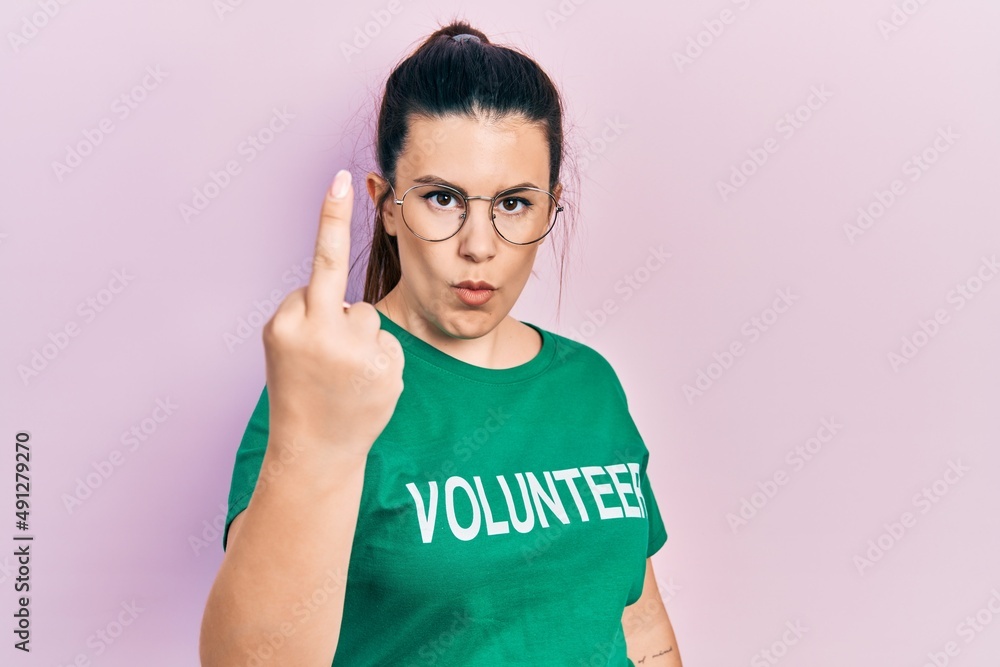Fototapeta premium Young hispanic woman wearing volunteer t shirt showing middle finger, impolite and rude fuck off expression