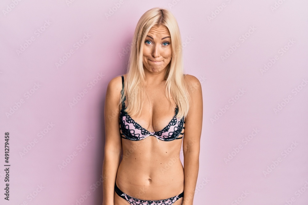 Obraz premium Young blonde woman wearing lingerie puffing cheeks with funny face. mouth inflated with air, crazy expression.